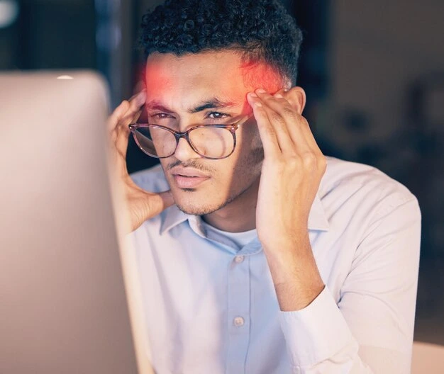 A person working on a computer with visible signs of eye strain (headache, red eyes).