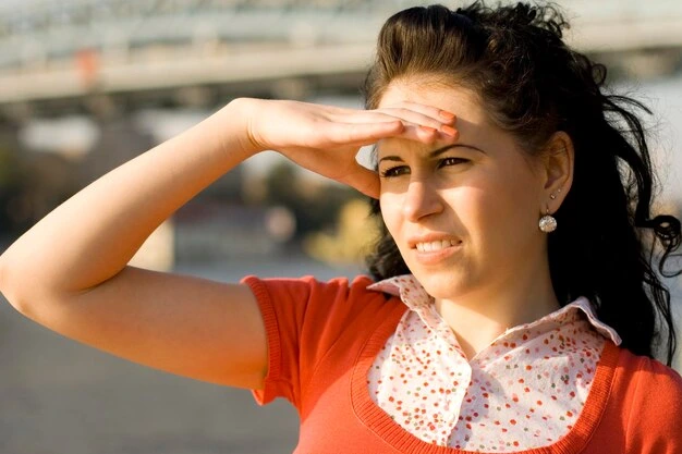 person shielding their eyes from bright sunlight or dust